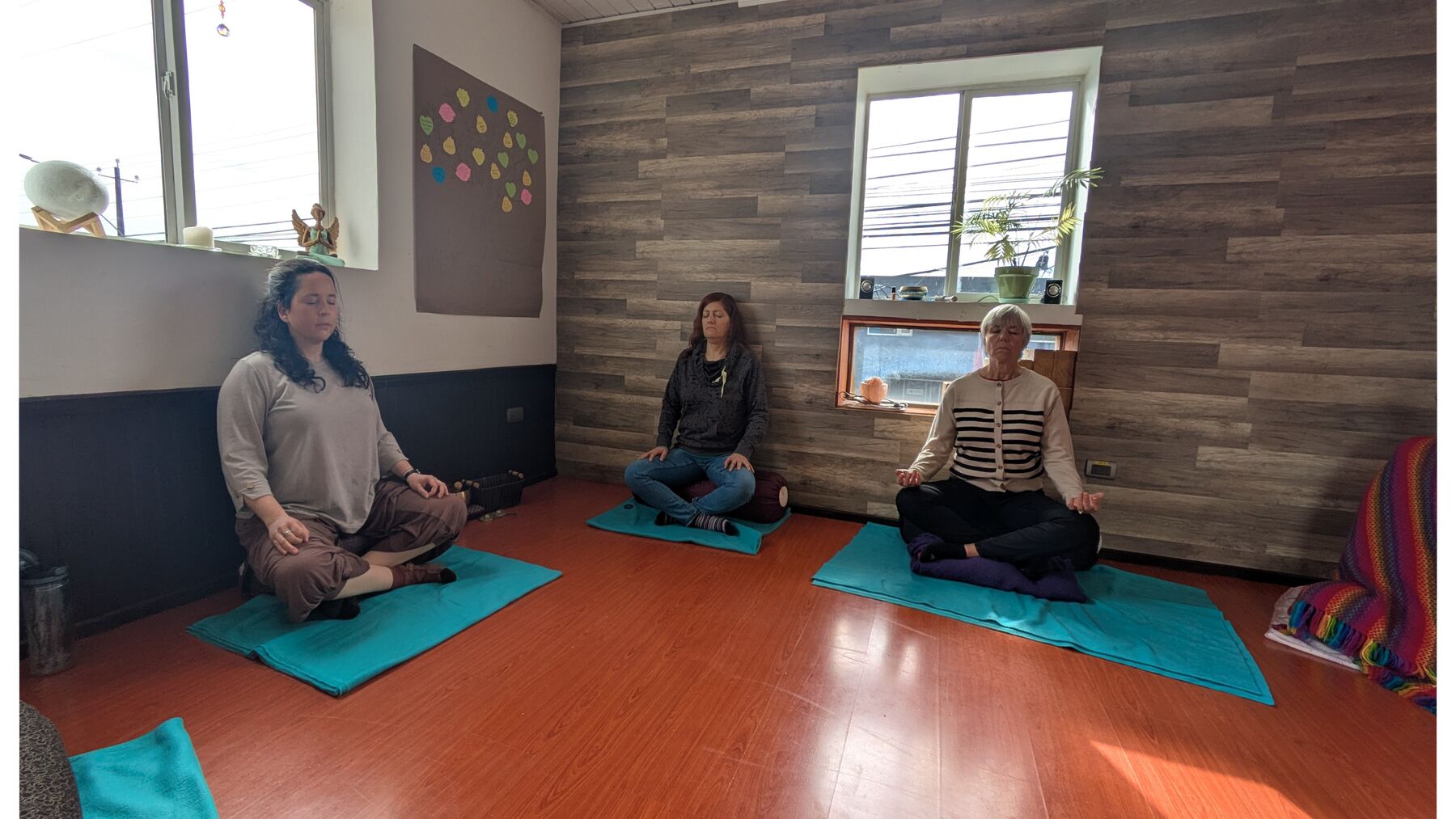 Tres personas meditando sobre colchonetas en una sala luminosa